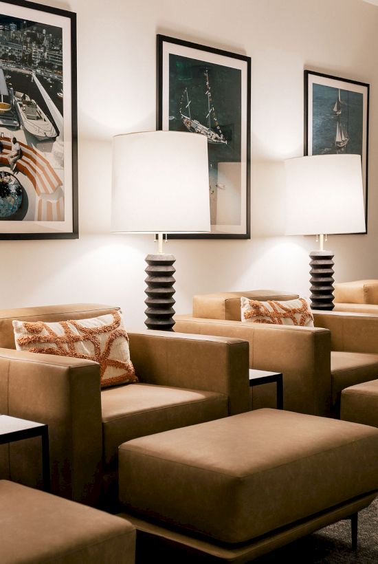 A cozy lounge with tan armchairs, matching ottomans, tall table lamps, framed photos, and built-in white cabinets in a calming waiting area.