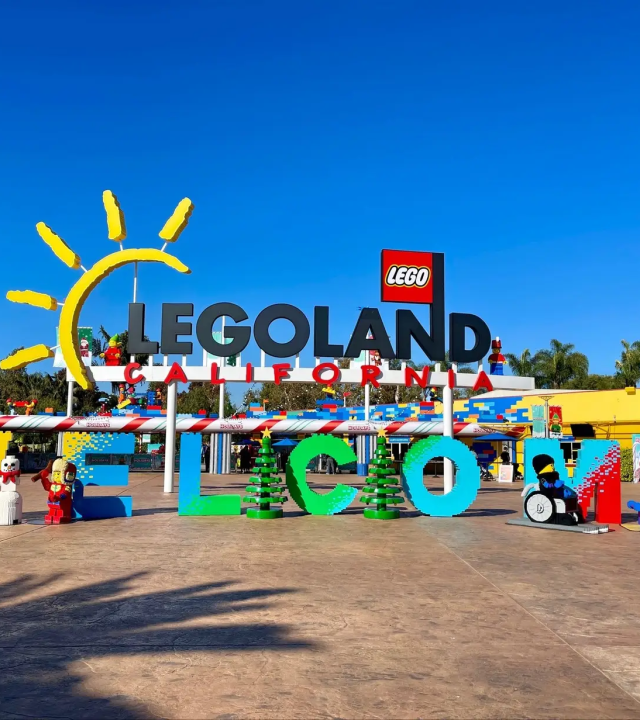 A LEGO Land California entrance sign with colorful LEGO figures and a huge “LEGO LAND” display under a blue sky.