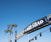A roller-coaster track and sign reading “CARL’S BAD” under a bright blue sky with palm trees.