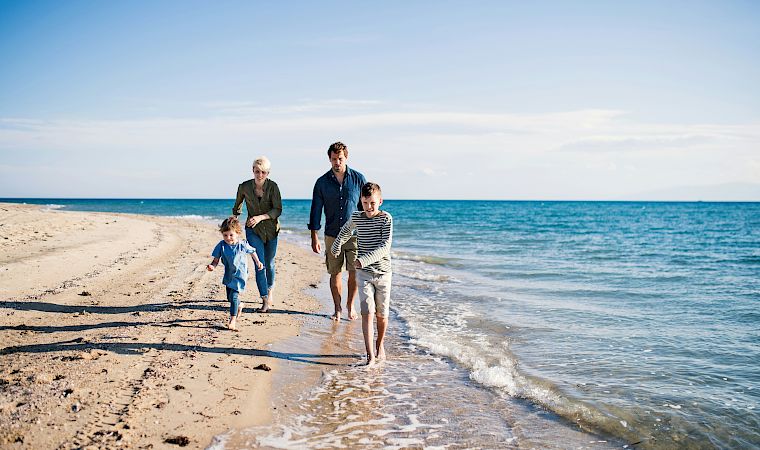 A family of four walks along a sunny beach, waves lapping at their feet, as they enjoy a seaside stroll together.